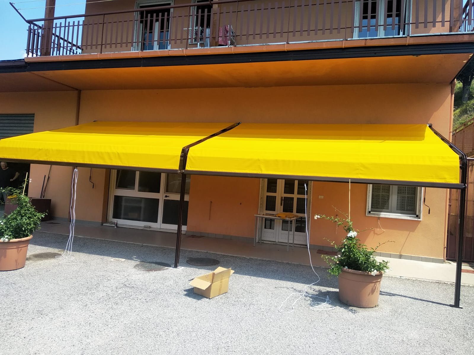 Edificio arancione con una tenda da sole giallo brillante e piante in vaso su un patio di ghiaia.