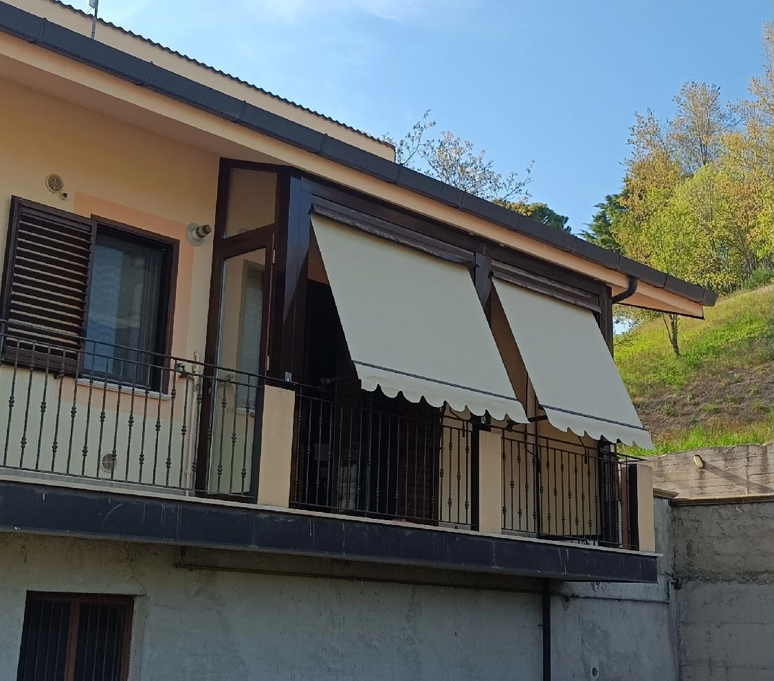 Casa a due piani con finestre aperte e tende da sole beige in una giornata di sole.