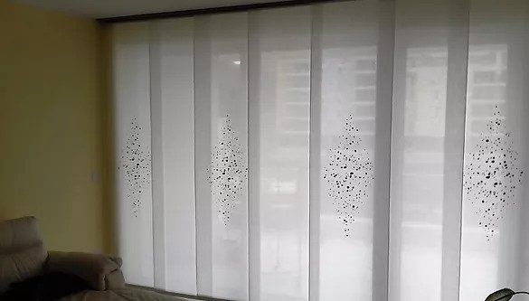 In una stanza dalla luce soffusa, ampie finestre sono coperte da tende bianche trasparenti con un motivo a pois.