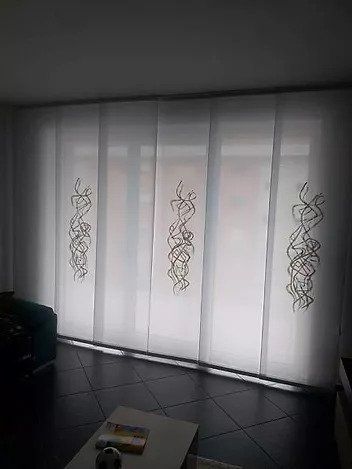 Tende bianche trasparenti con ricami floreali che filtrano la luce in una stanza poco illuminata