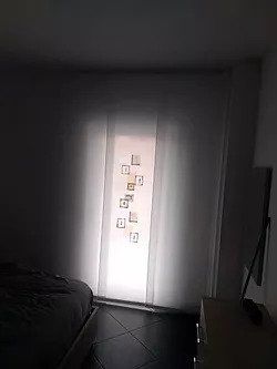 Camera da letto in penombra, illuminata dalla luce del sole che filtra attraverso tende trasparenti e con piccoli quadri sul davanzale della finestra.