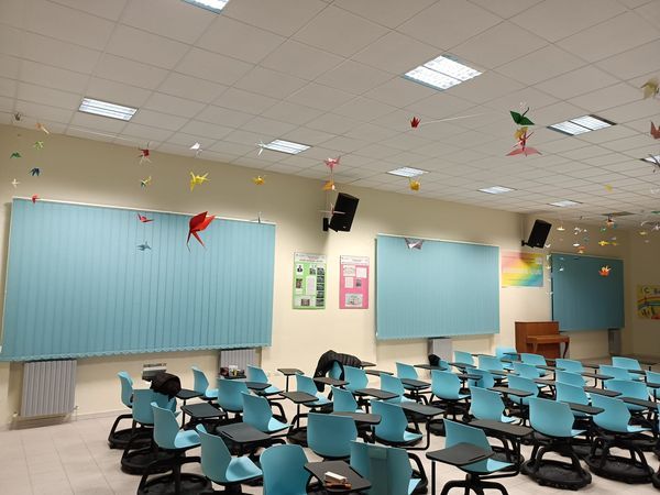 Aula vuota con sedie blu, banchi, bacheche e decorazioni di carta appese al soffitto.