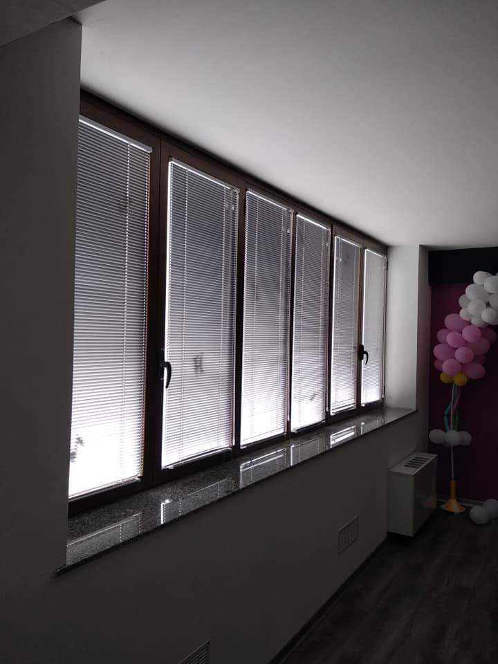 Corridoio buio con finestre smerigliate, pavimento scuro e decorazioni di palloncini rosa e bianchi in fondo.