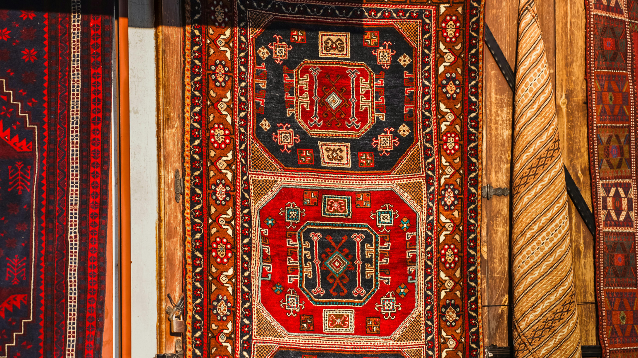 Colorful patterned woven rug with red, gold, and black geometric designs and fringe edges