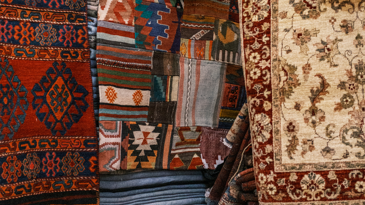 Patterned woven rugs in red, blue, beige, and brown hanging side by side.