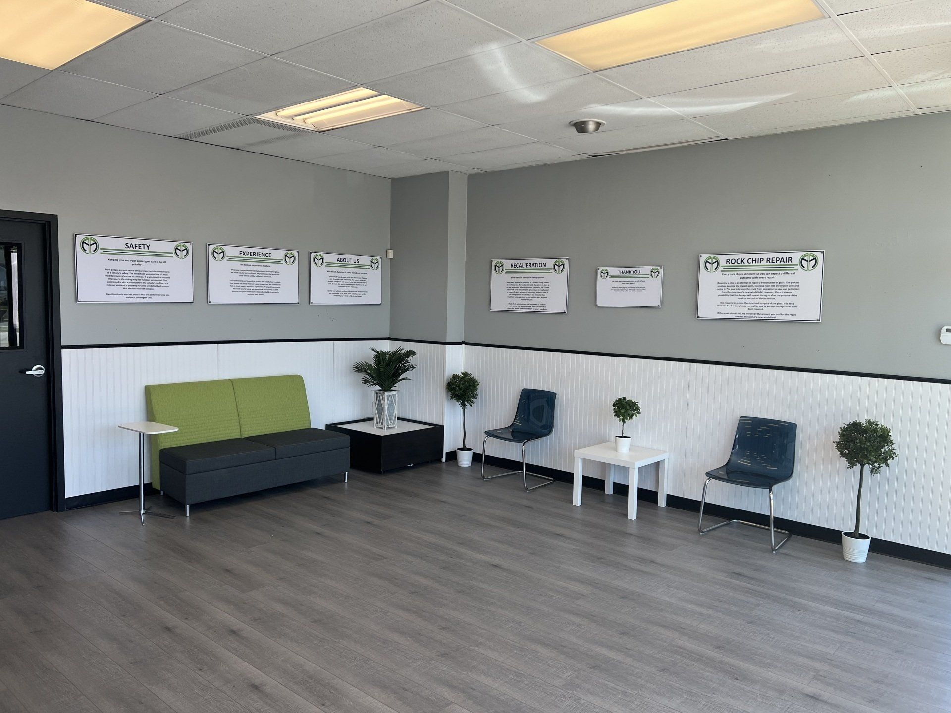 Empty waiting room with gray walls, green bench, chairs, and potted plants under fluorescent lights