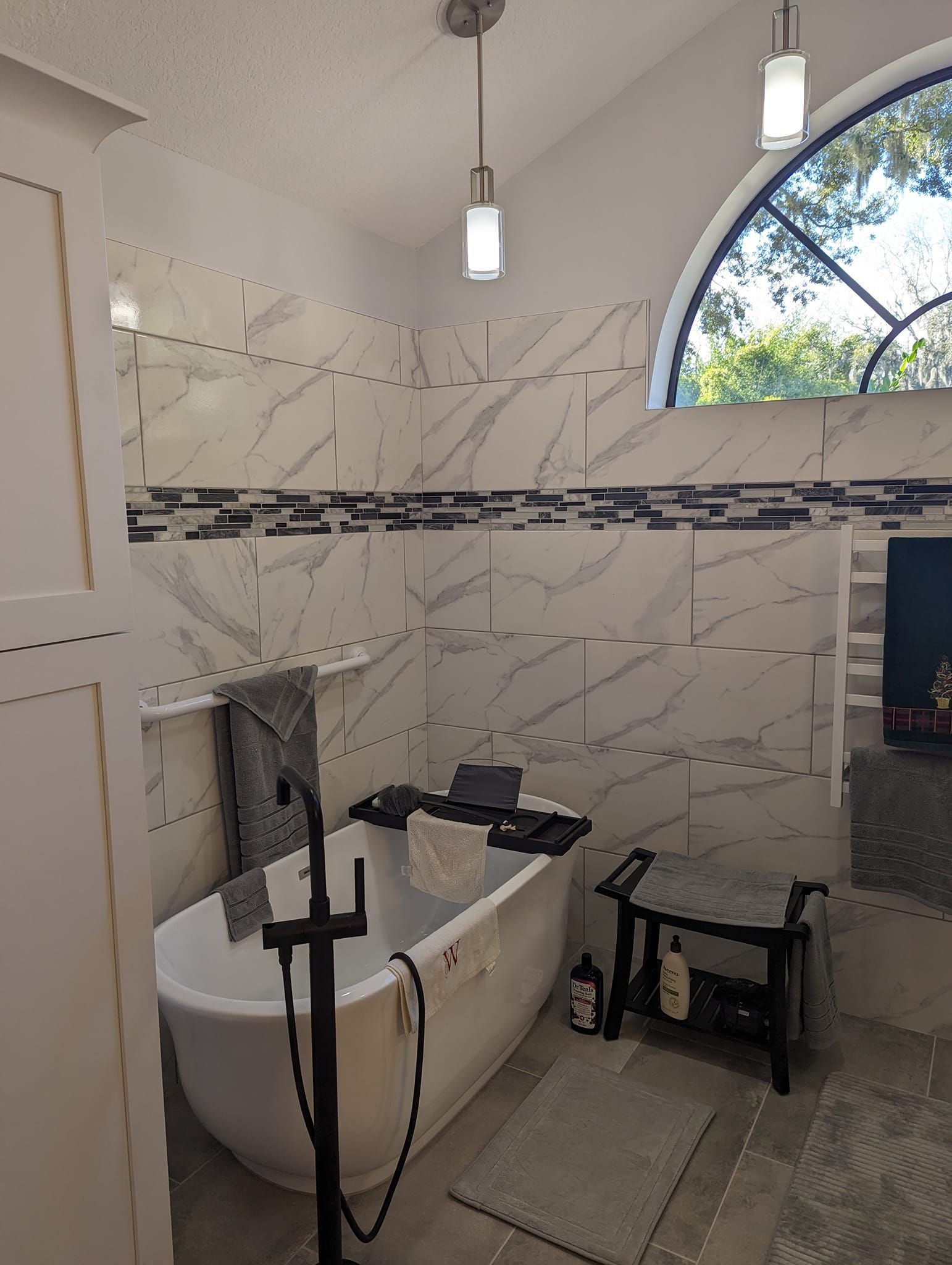 Modern bathroom with freestanding tub, white and gray tile, and arched window.