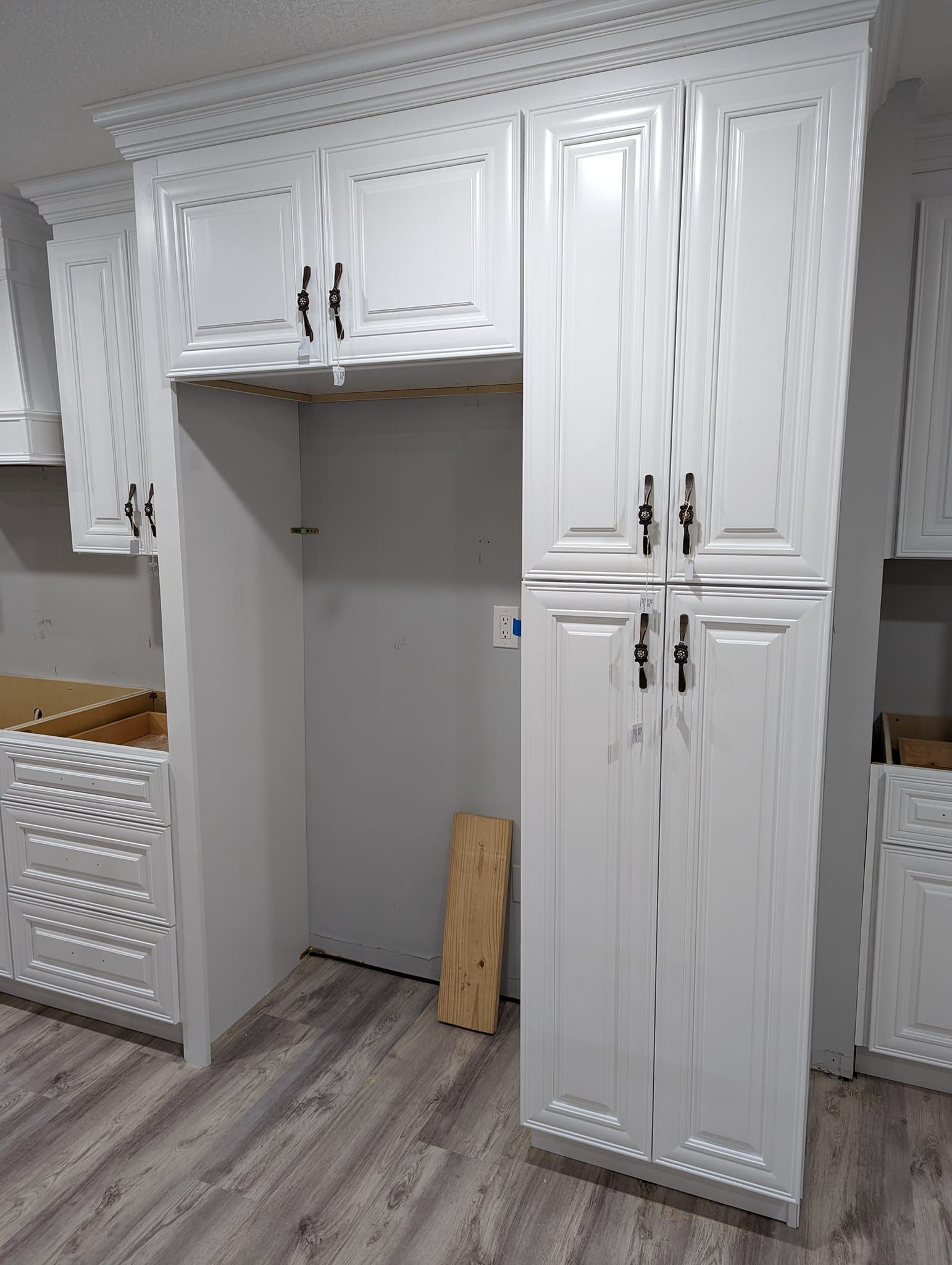 White kitchen cabinets with crown molding, refrigerator space, and drawers, partially installed.