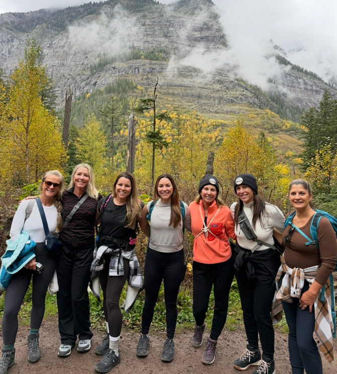 Seven hikers posing on a trail, with autumn trees and misty mountains in the background.