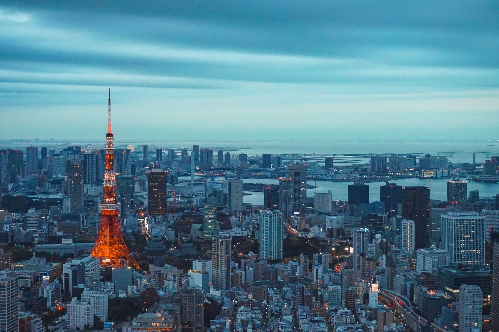 Tokyo skyline at dusk with the illuminated Tokyo Tower glowing orange among blue-gray high-rises