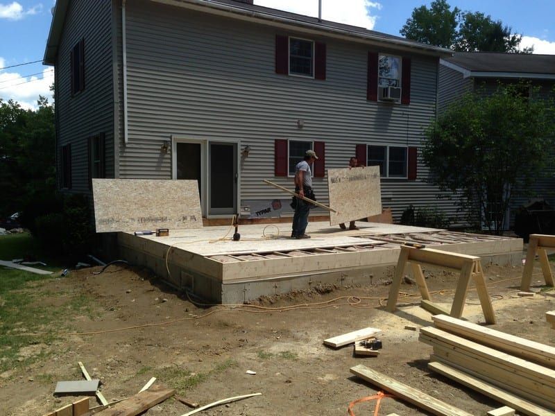 A man is carrying a piece of plywood in front of a house