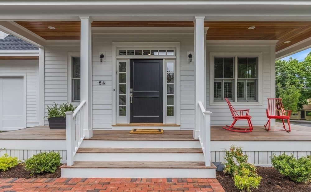 A white house with a black door and a porch with rocking chairs.