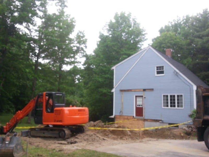 An orange excavator is parked in front of a blue house