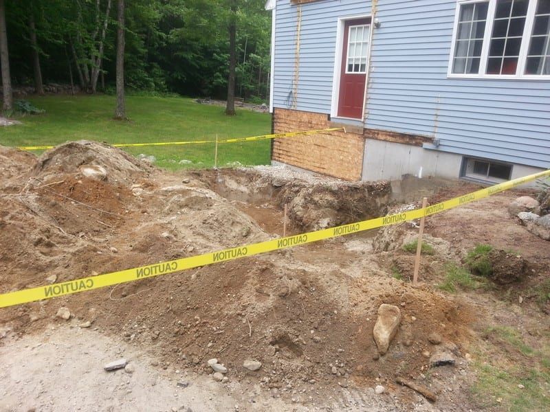 A pile of dirt is surrounded by caution tape in front of a house.