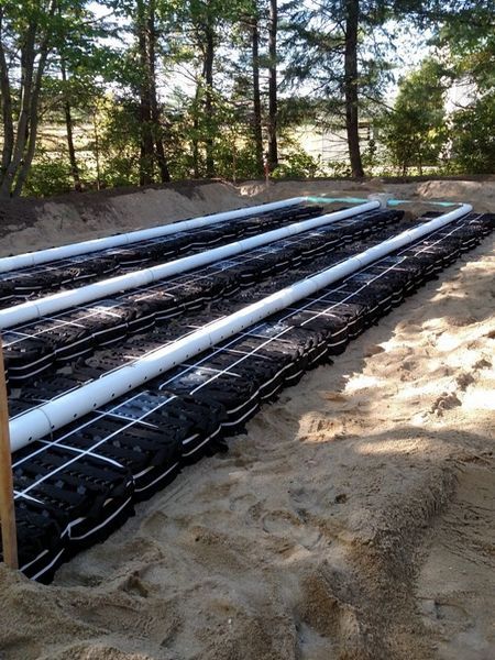 A septic system is being built in the dirt with trees in the background.