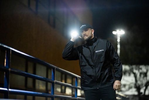 Security guard with flashlight patrolling residential parking lot at night in San Diego