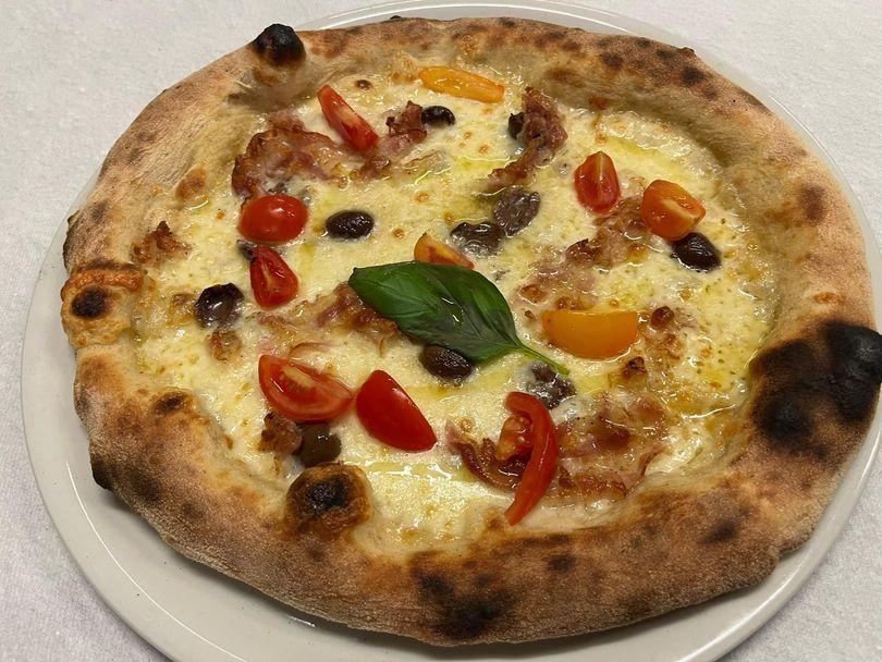 Pizza cotta nel forno a legna, condita con pomodorini, olive, peperoni e basilico, servita su un piatto bianco