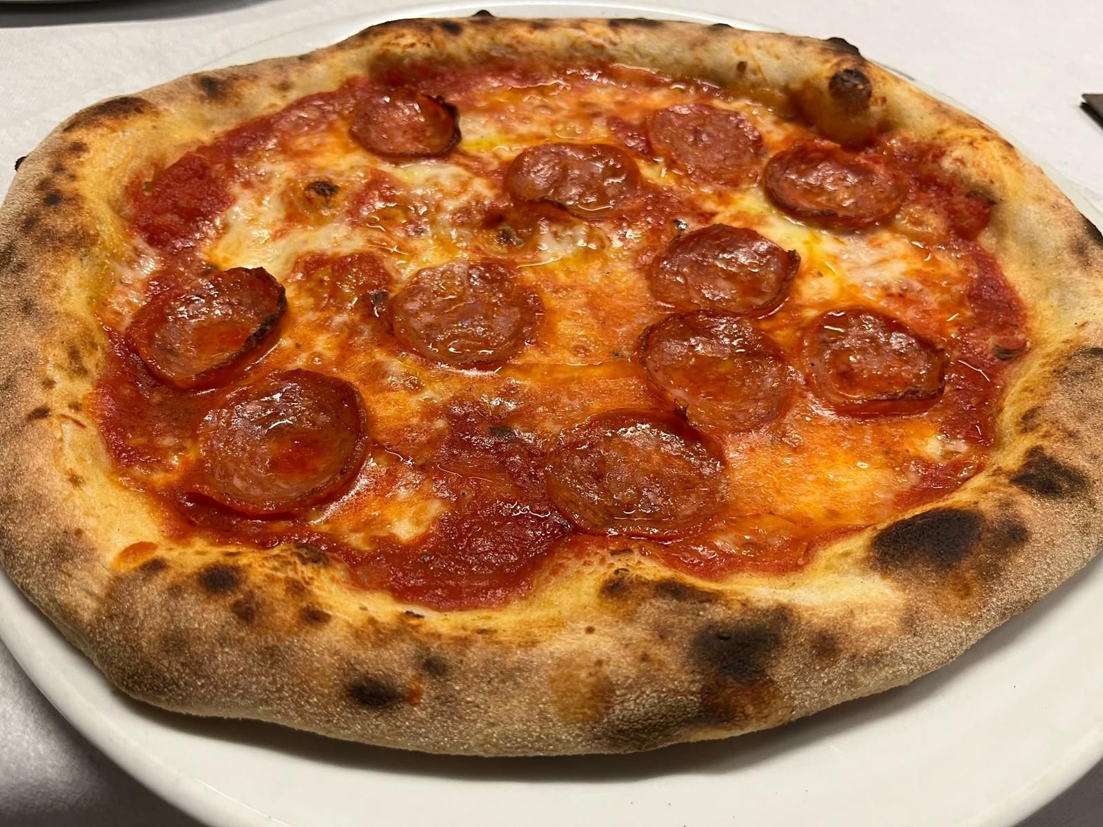 Pizza ai pepperoni su un piatto bianco, con la crosta dorata e croccante e il formaggio fuso