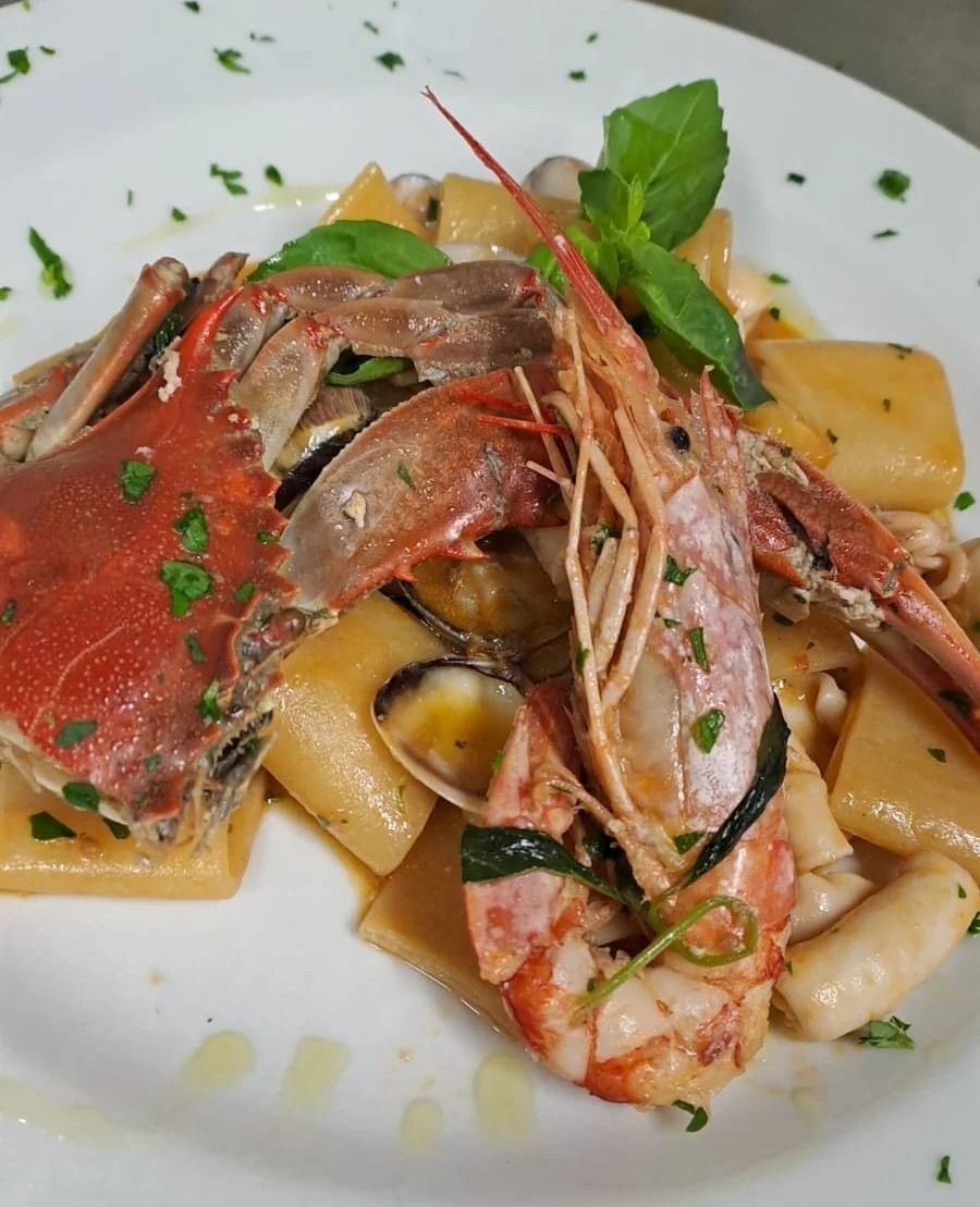 Pasta ai frutti di mare con chele di granchio, gamberi e basilico, servita su un piatto bianco