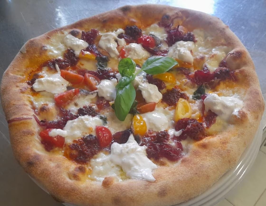 Pizza con formaggio fuso, pomodorini, basilico e salsa rossa, servita su un piatto