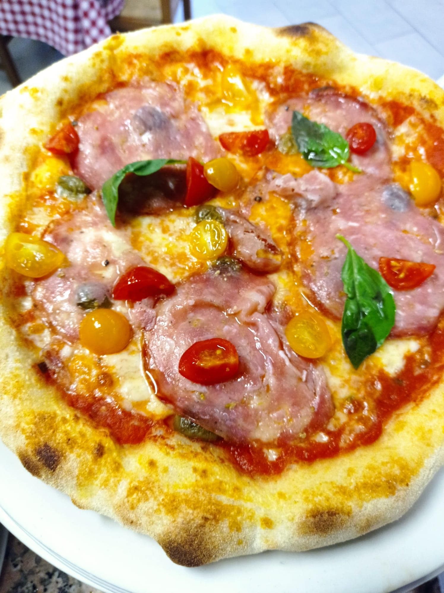 Piccola pizza con prosciutto, pomodorini, basilico e formaggio fuso, servita su un piatto bianco