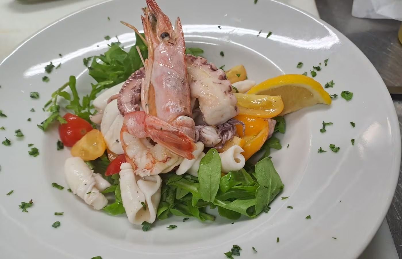 Insalata di mare con gamberetti, polpo, pomodorini e verdure su un piatto bianco