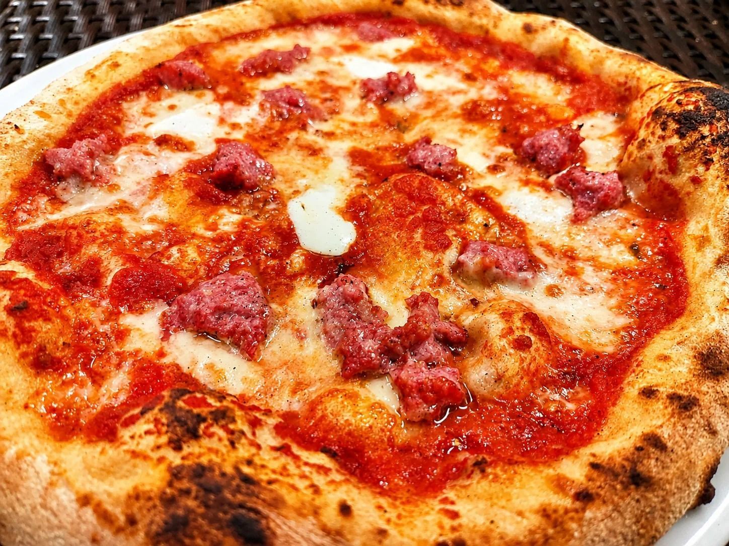 Primo piano di una pizza al formaggio e pomodoro con il bordo dorato e leggermente bruciacchiato