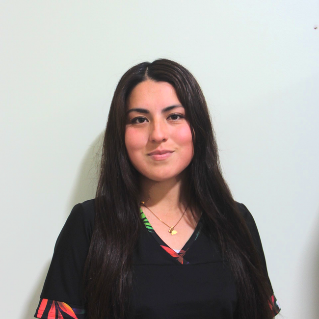 Mujer con cabello largo y oscuro, vestida con una blusa negra, sonriendo contra un fondo claro liso.