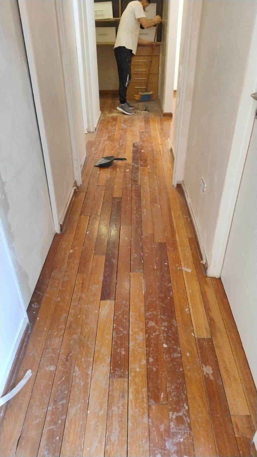 Pasillo estrecho con suelo de madera noble que están decapando; una persona trabaja al fondo.