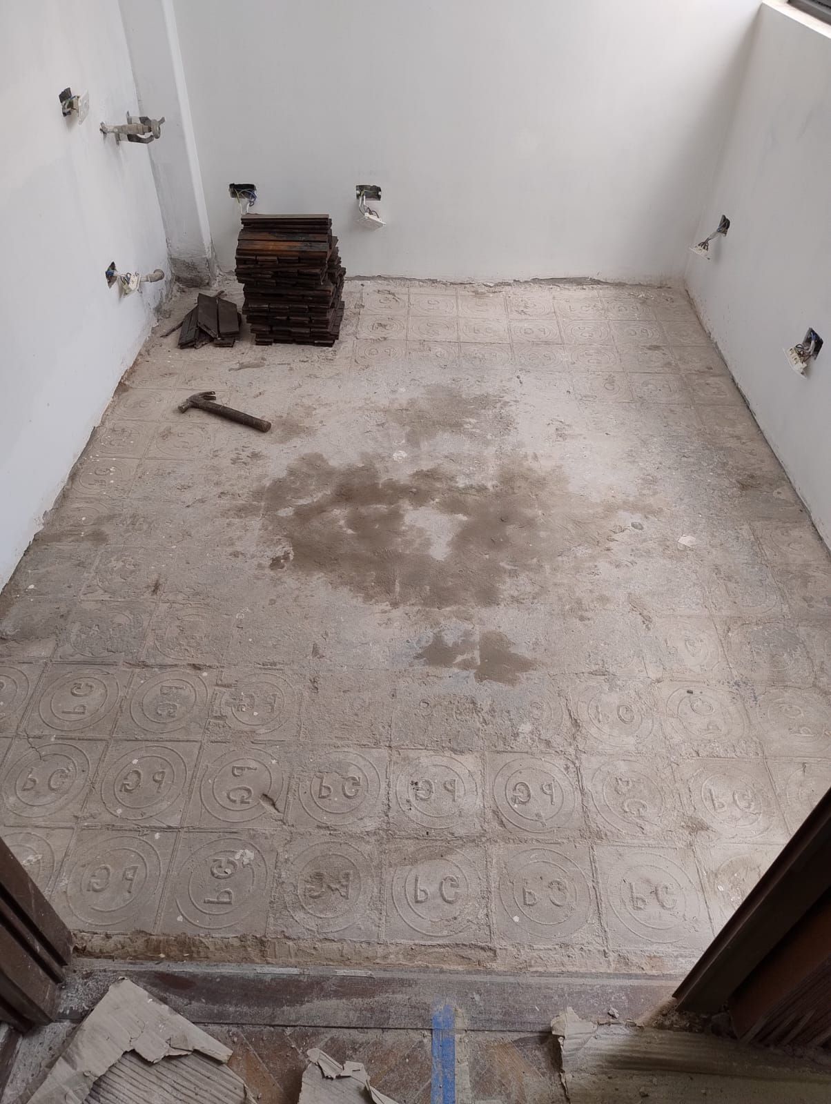 Habitación vacía sin terminar con suelo de hormigón visto, paredes blancas y una pequeña pila de materiales en una esquina.