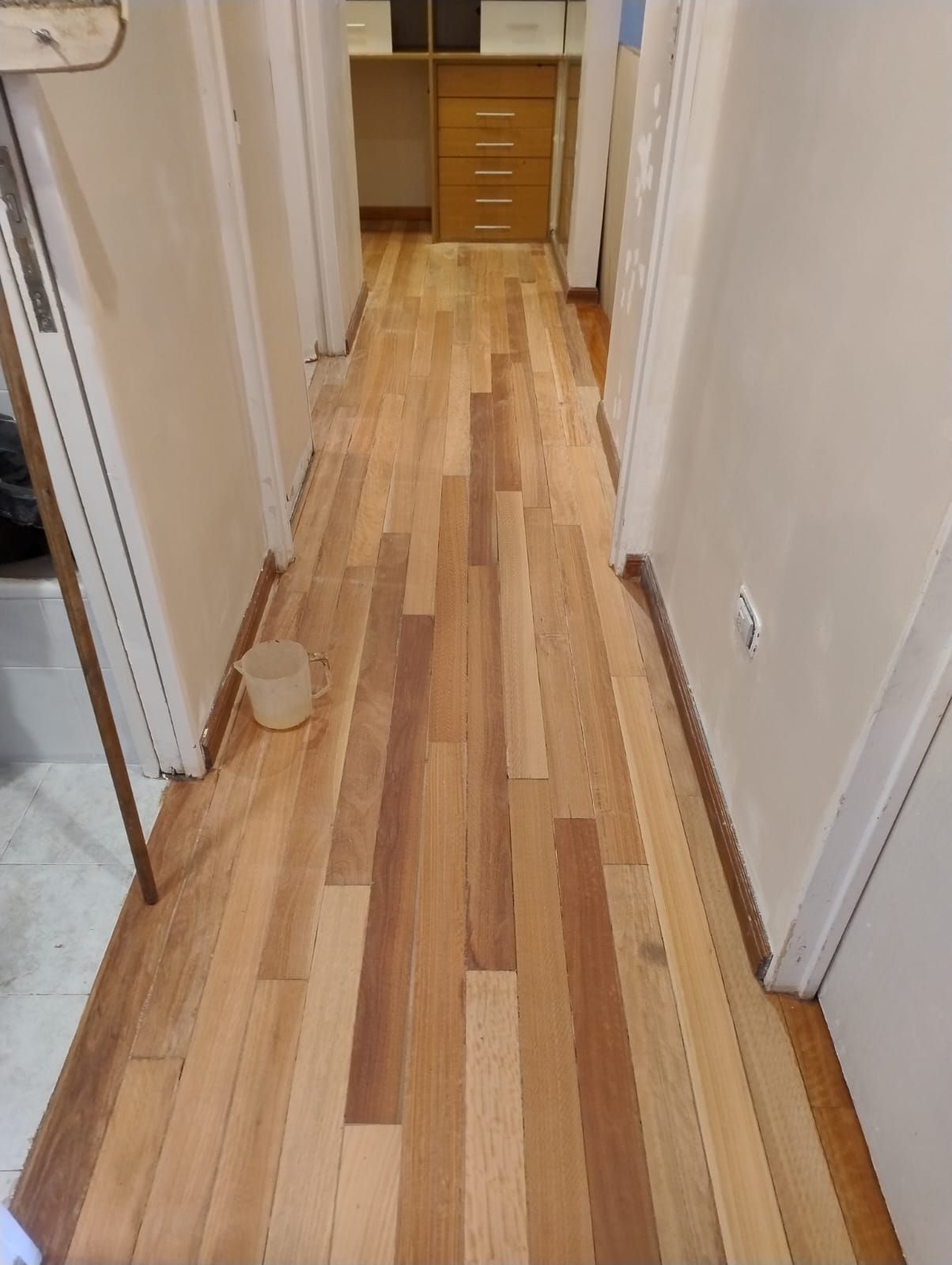 Pasillo estrecho con suelo de madera clara, paredes blancas y una cómoda al final.