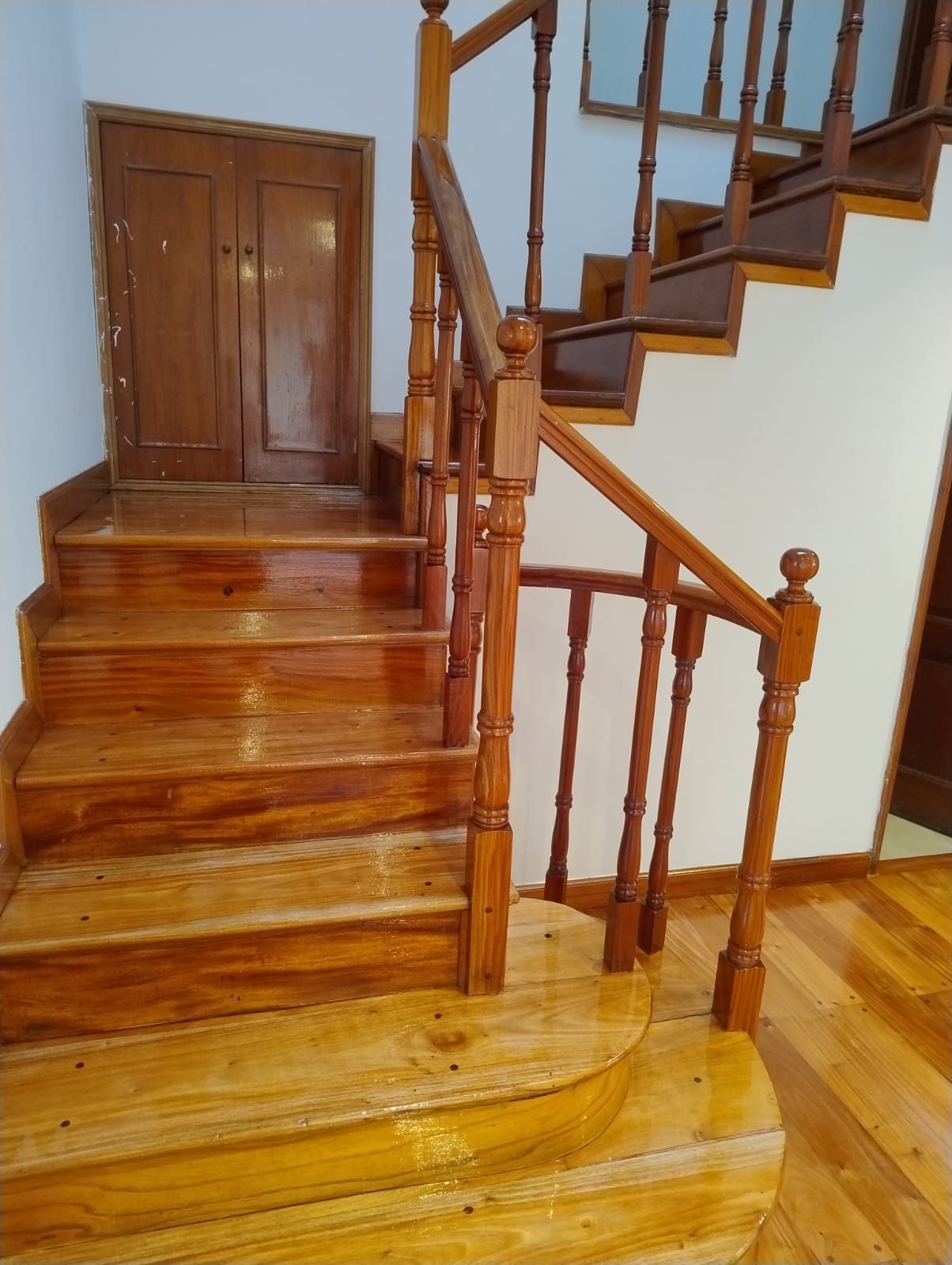 Escalera de madera con escalones y barandilla pulidos junto a un pequeño armario en un pasillo.