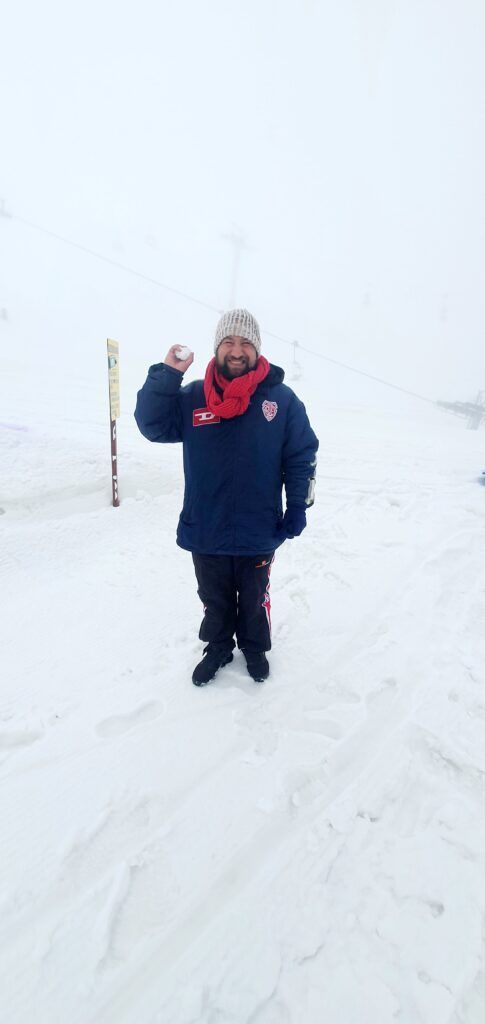 A man in a blue jacket and scarf is standing in the snow.