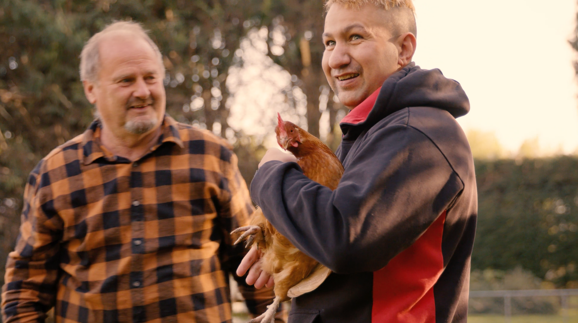 A man is holding a chicken in his arms while another man looks on.