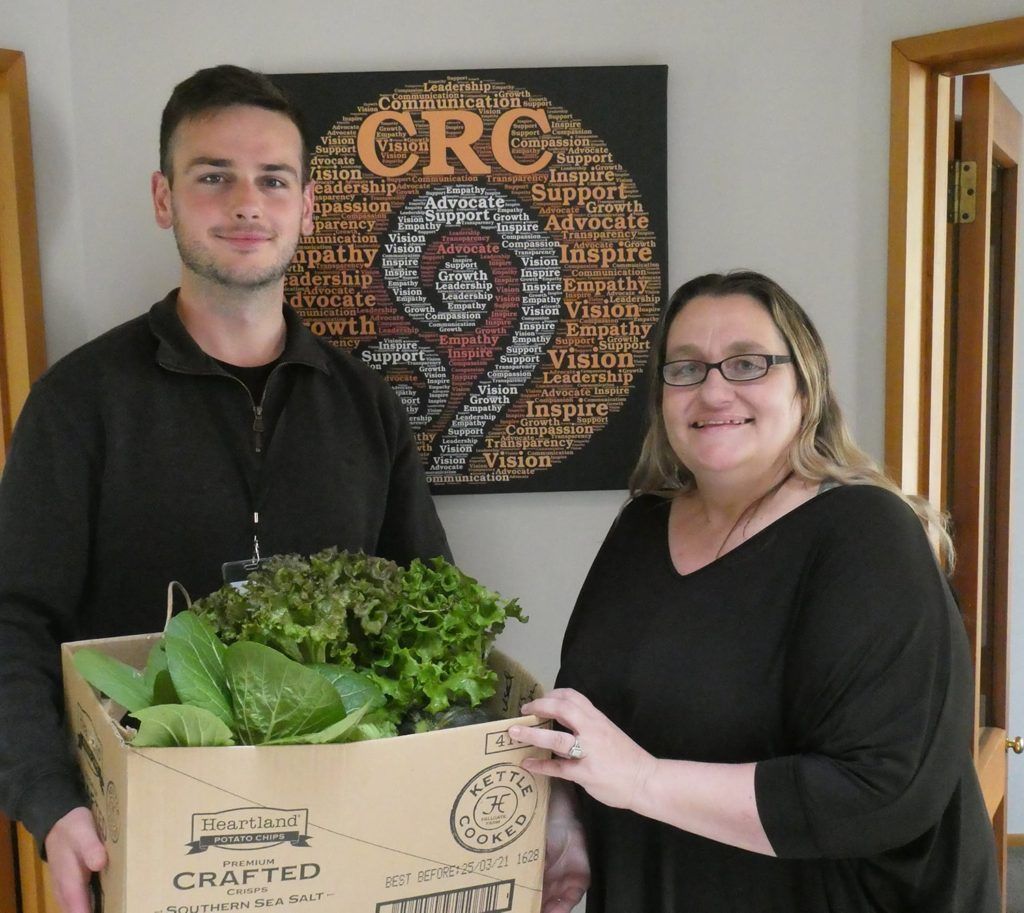 A man and a woman are holding a box of lettuce in front of a sign that says crc