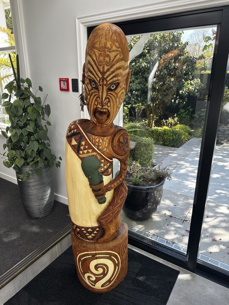 A wooden statue of a man is sitting in front of a glass door.