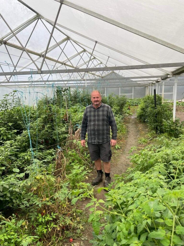 A man is standing in a greenhouse surrounded by plants.