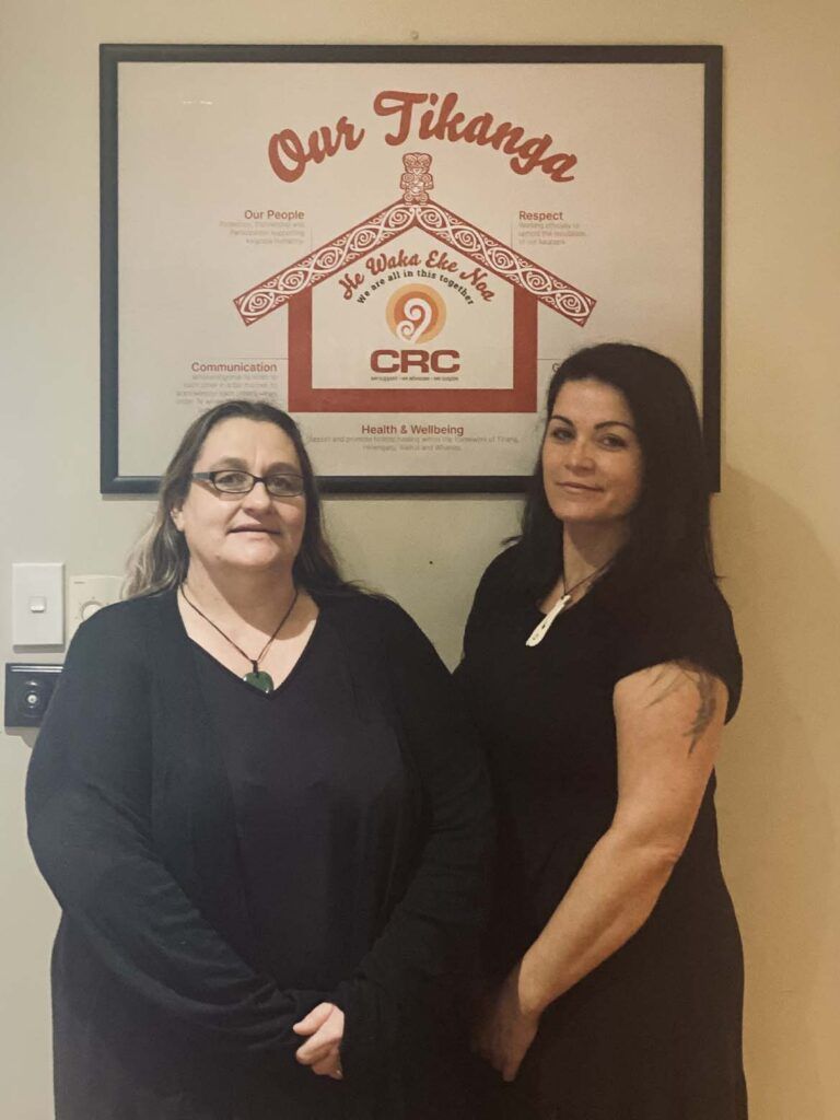 Two women are posing for a picture in front of a sign that says our tikanga.