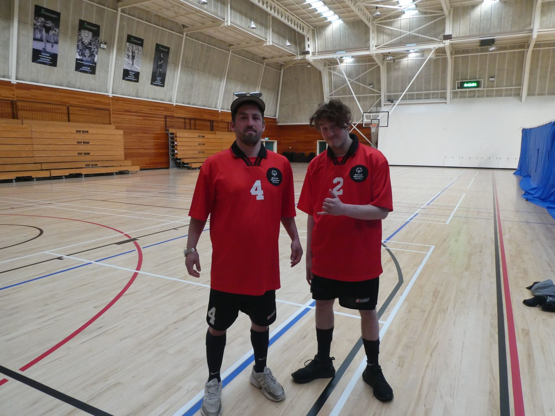 Two men standing on a basketball court wearing red jerseys with the number 4 and 2 on them