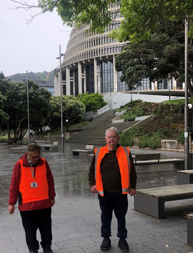 Two men wearing orange vests are walking down a sidewalk