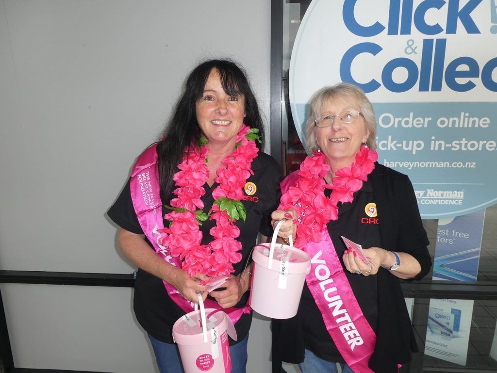 Two women standing next to each other wearing sashes that say volunteer