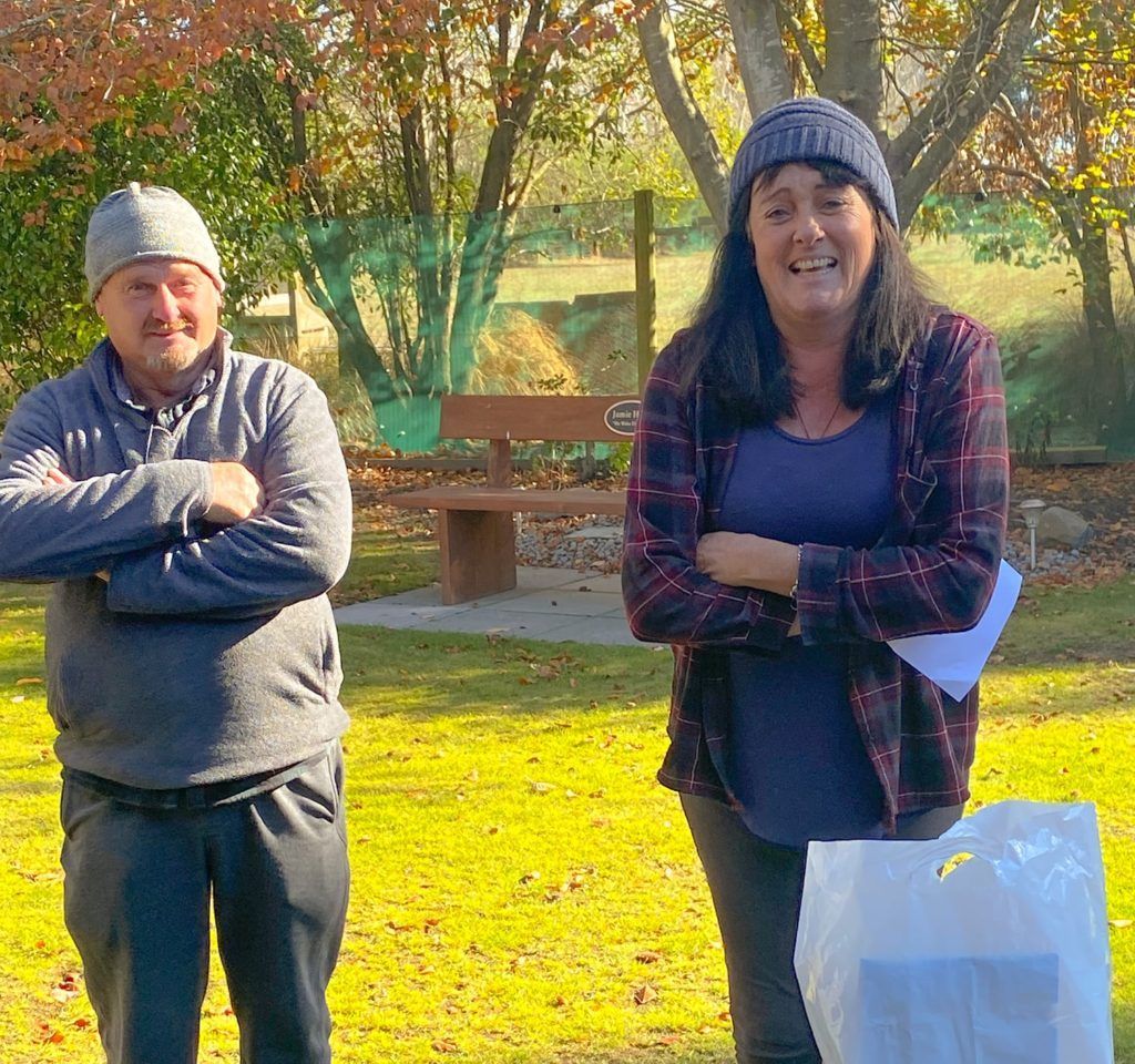 A man and a woman are standing next to each other in a park.