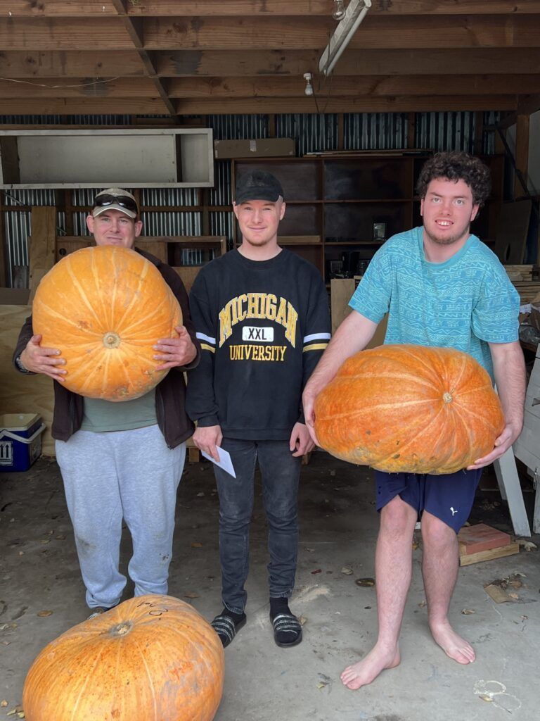 Three people are standing next to each other holding large pumpkins.
