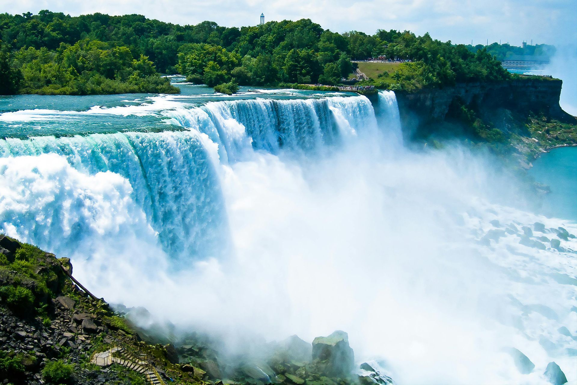 Niagara Falls cascading water, lush green trees, and a bright blue sky.