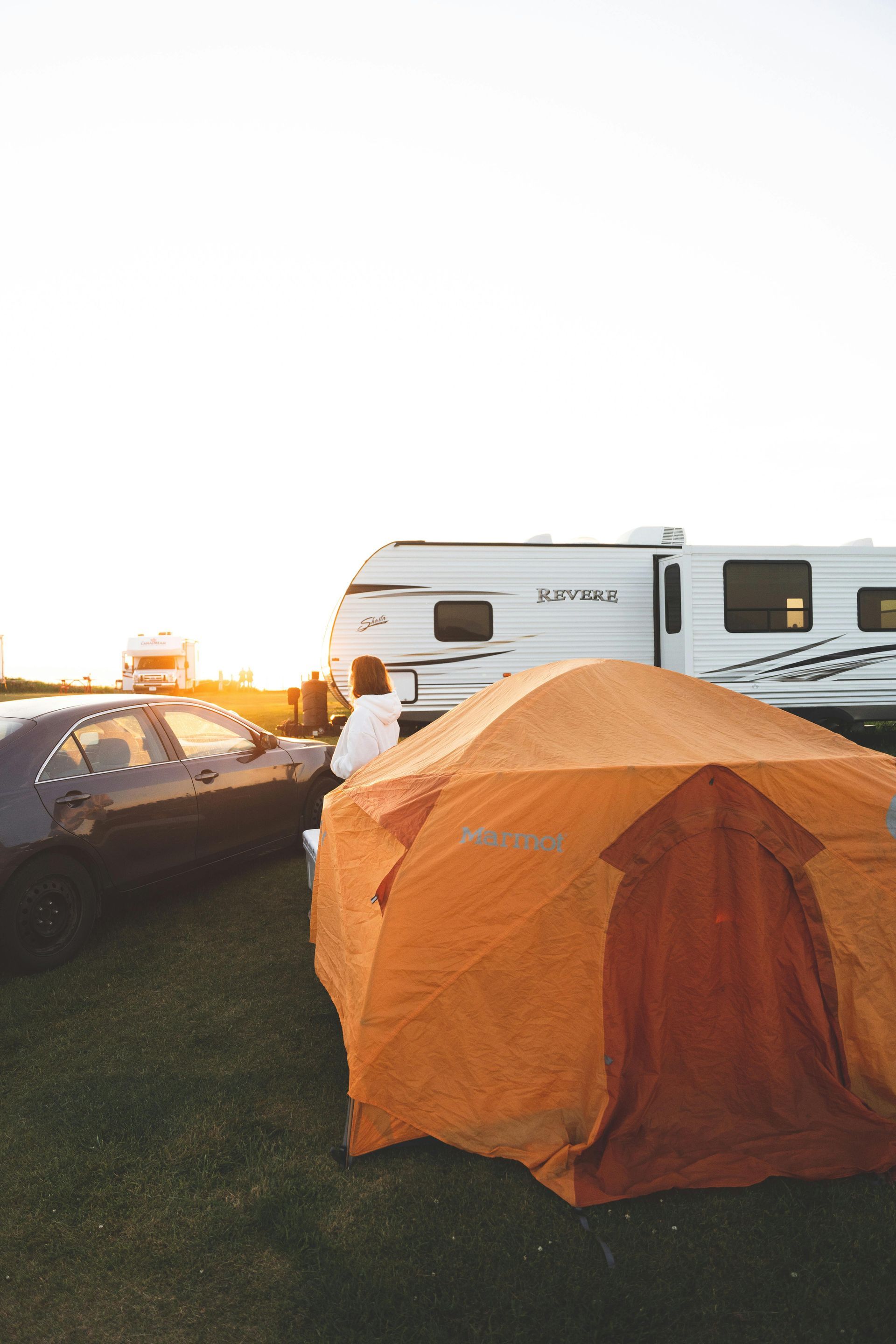 Orange tent at a campsite beside a trailer and car at sunset