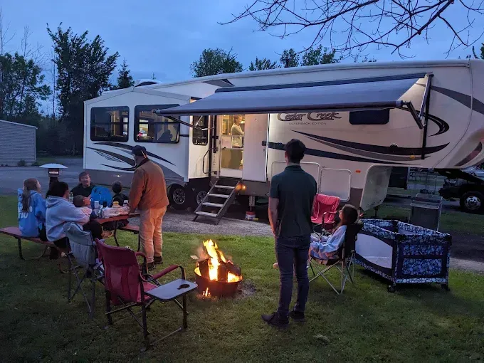 Family camping: People around a campfire next to an RV, set at dusk.