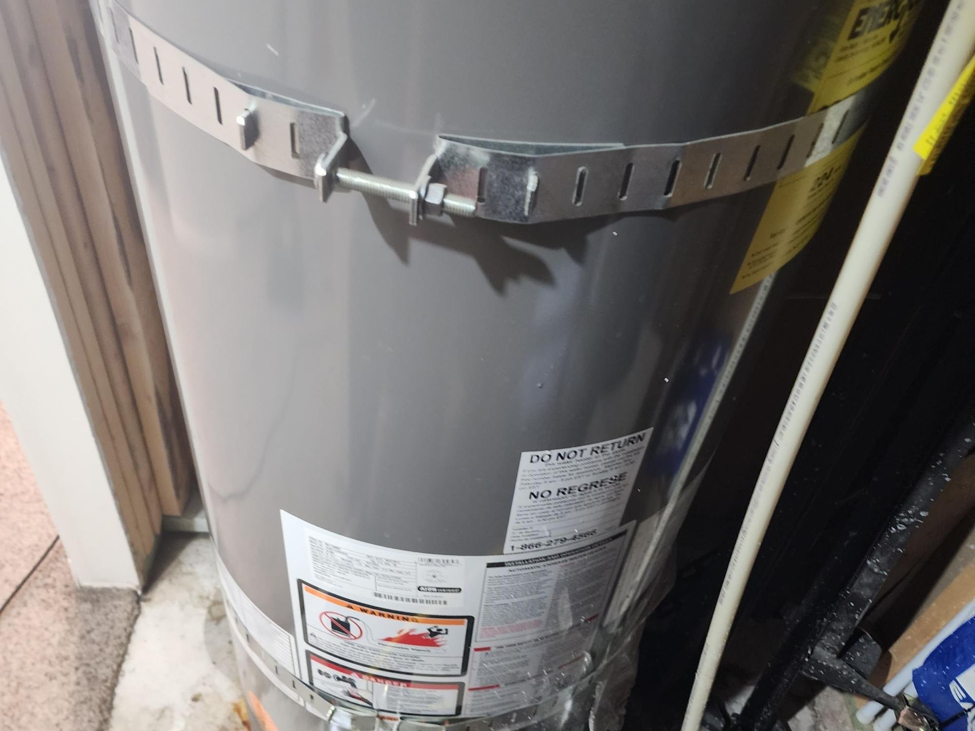 A gray water heater secured by a metal strap in a utility room.