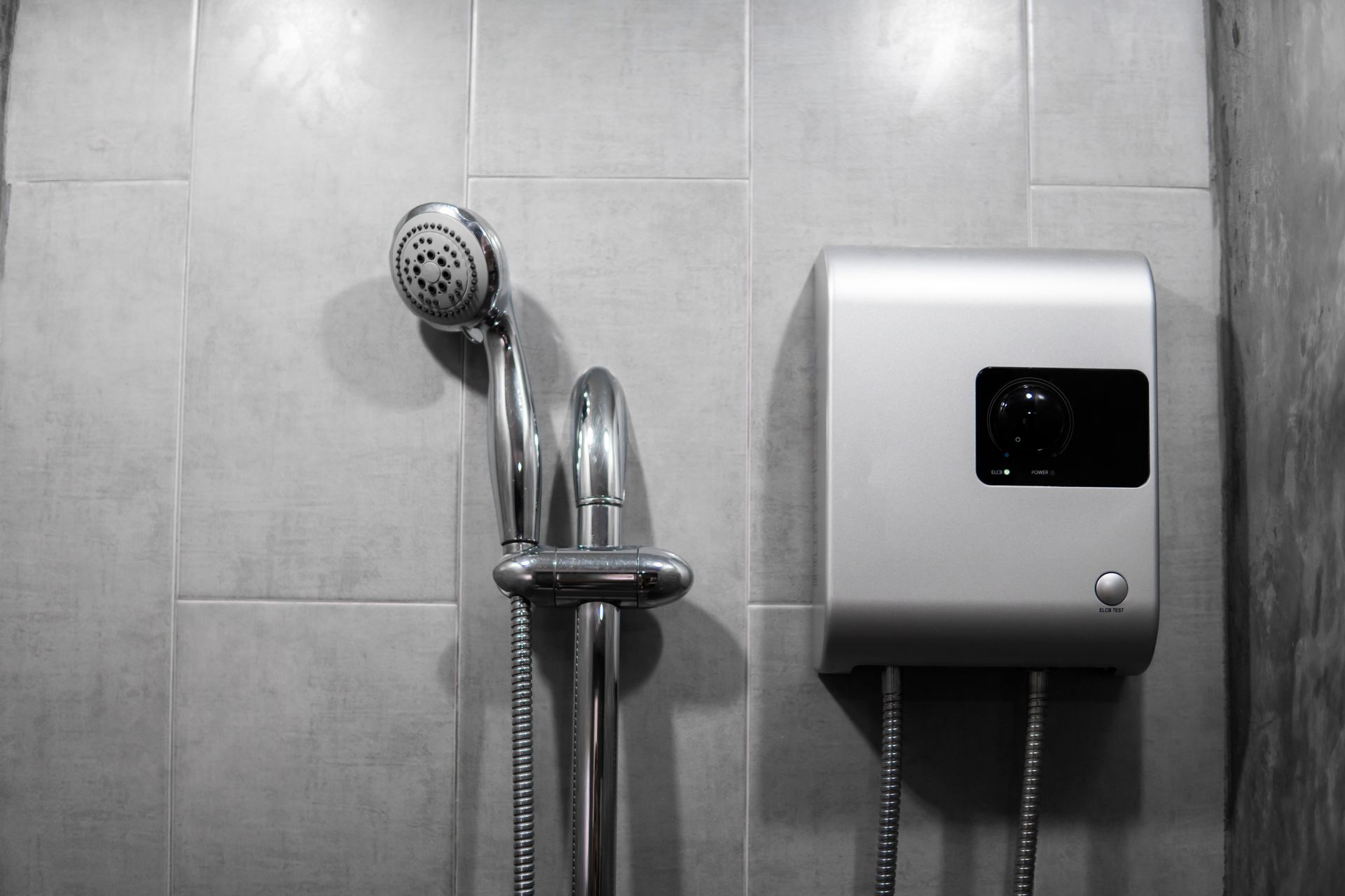 Showerhead and silver water heater mounted on tiled wall.