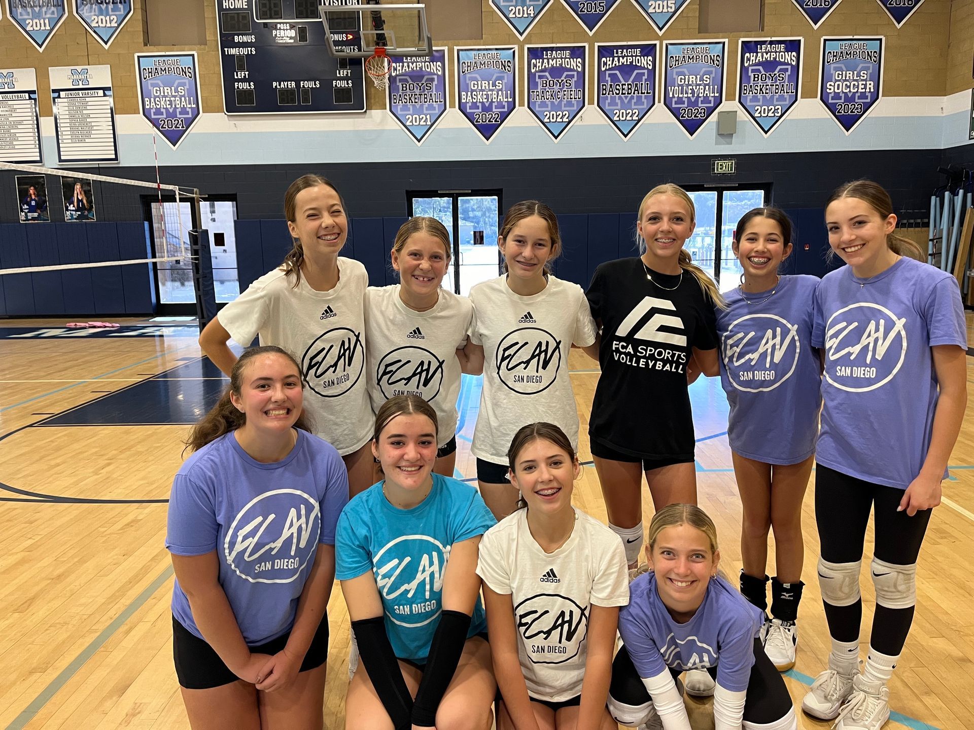 Volleyball team in teal jerseys posing for a group photo against a white backdrop