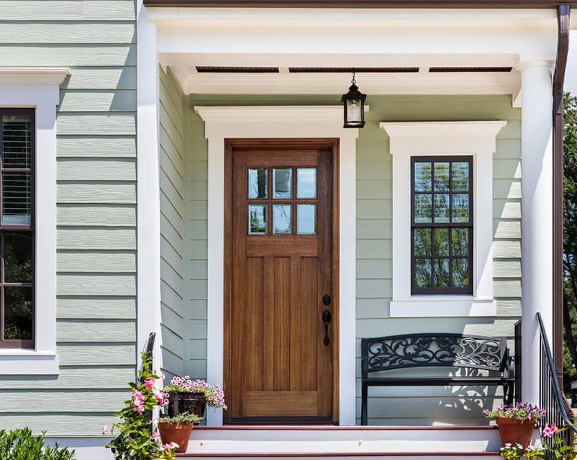 Front porch with a wooden door, white columns, hanging lantern, and black bench on a light blue house.